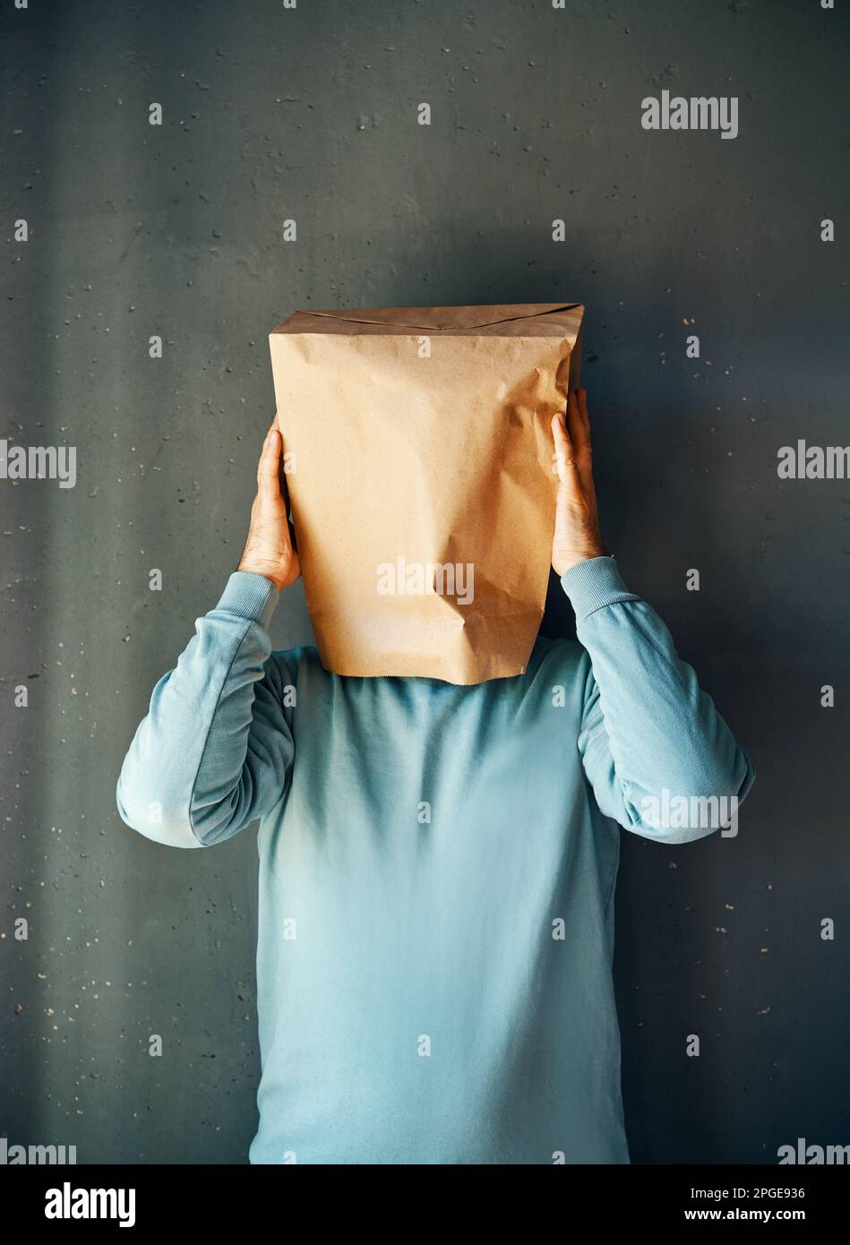 Upset man with a paper bag on head touching temples, suffering from strong tension headache over gray background. Emotion concept Stock Photo