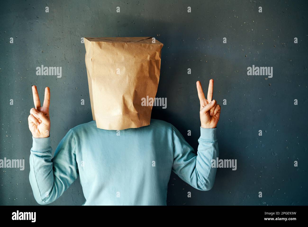 Happy positive man with a paper bag show victory sign over grey background. People emotion concept Stock Photo