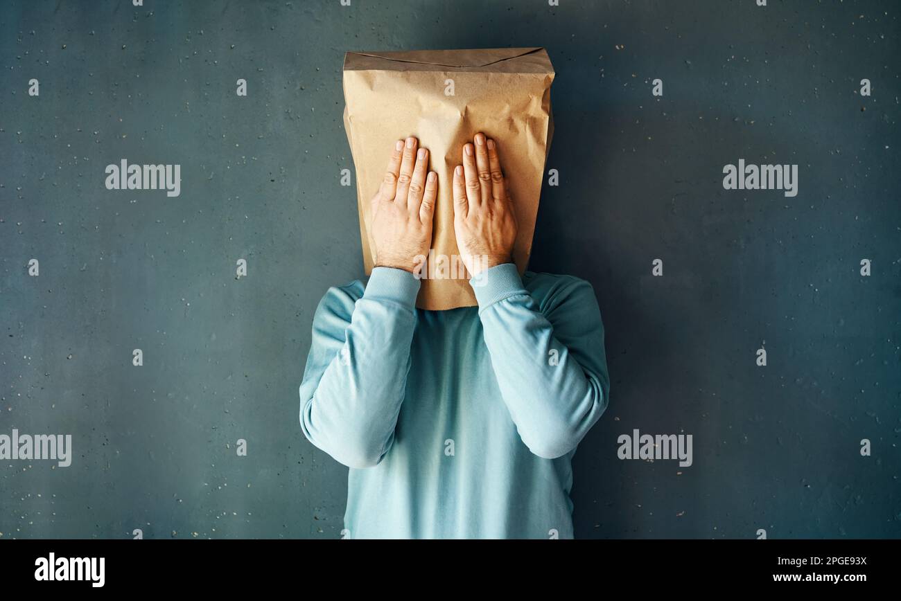 Man with a paper bag on head covering eyes with both hands over grey background. People emotion, fatigue, see no evil concept Stock Photo