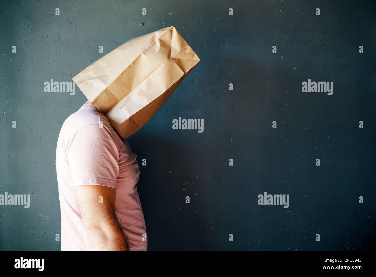 Profile view of upset man with a paper bag on head over gray background with copy space. People emotion concept Stock Photo