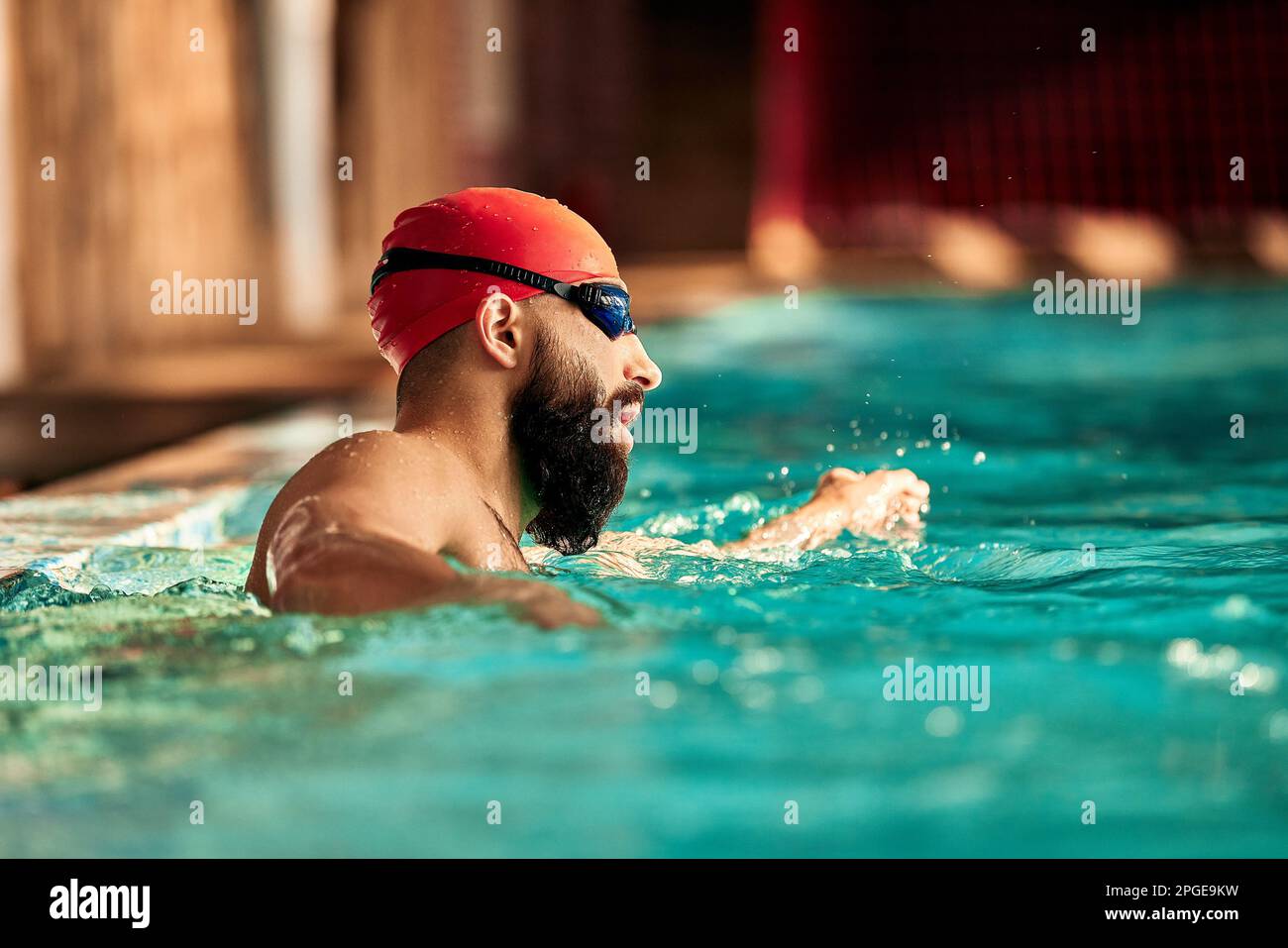 A young man swims crawl in the pool in a red cap and swimming goggles