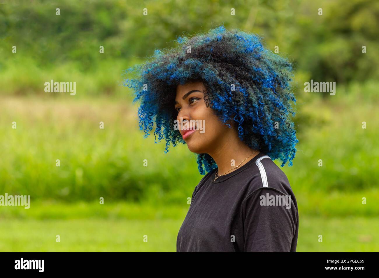 Goiania, Goias, Brazil – March 20, 2023: Photo of a young black woman with afro hair, dyed blue, with a slight smile on her face, in profile with blur Stock Photo