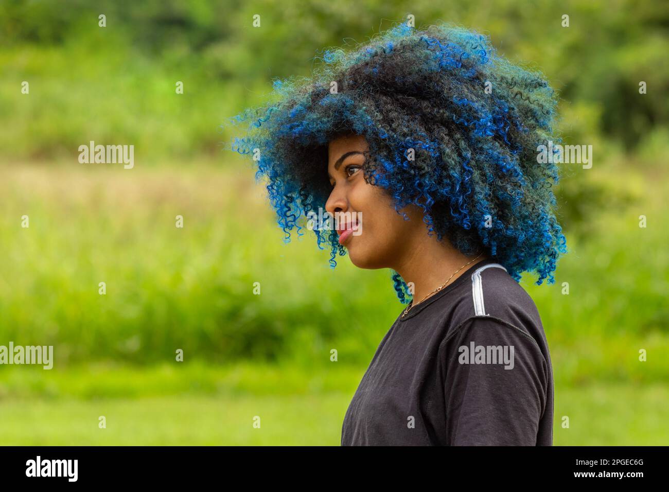 Goiania, Goias, Brazil – March 20, 2023: Photo of a young black woman with afro hair, dyed blue, with a slight smile on her face, in profile with blur Stock Photo