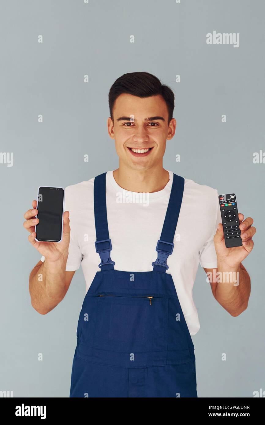 TV remote controller and smartphone. Male worker in blue uniform