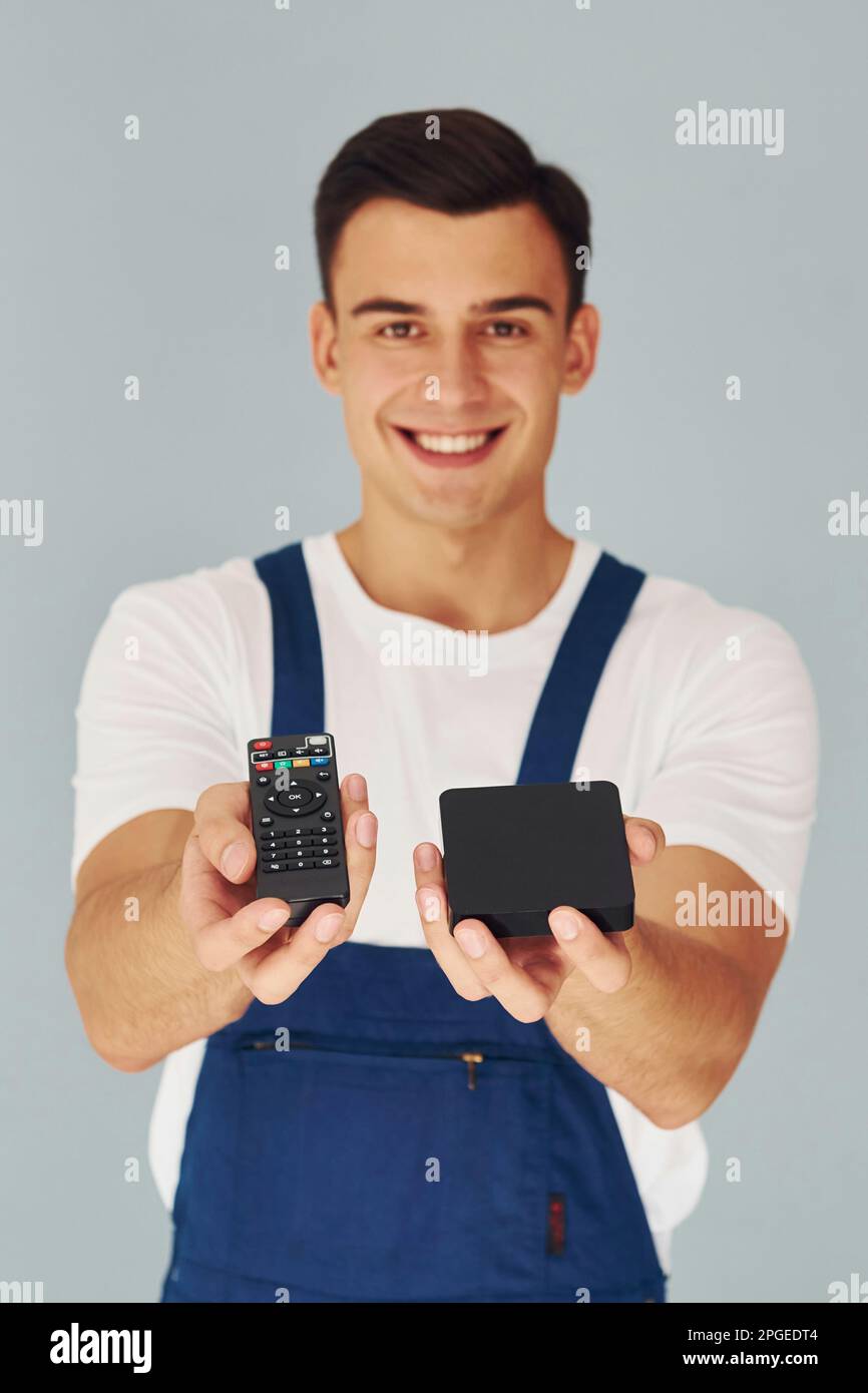 TV remote controller and smartphone. Male worker in blue uniform