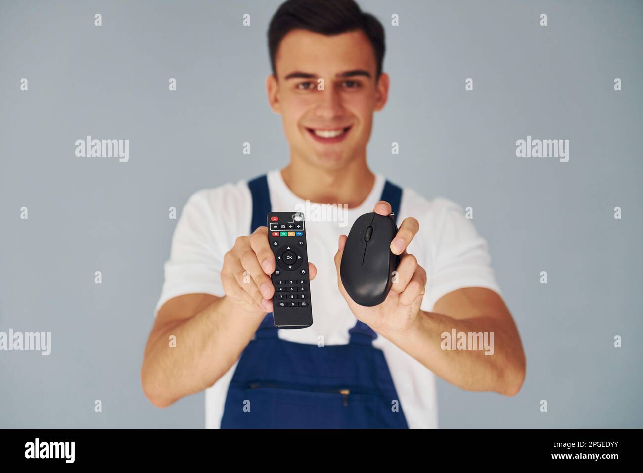 TV remote controller and computer mouse. Male worker in blue uniform