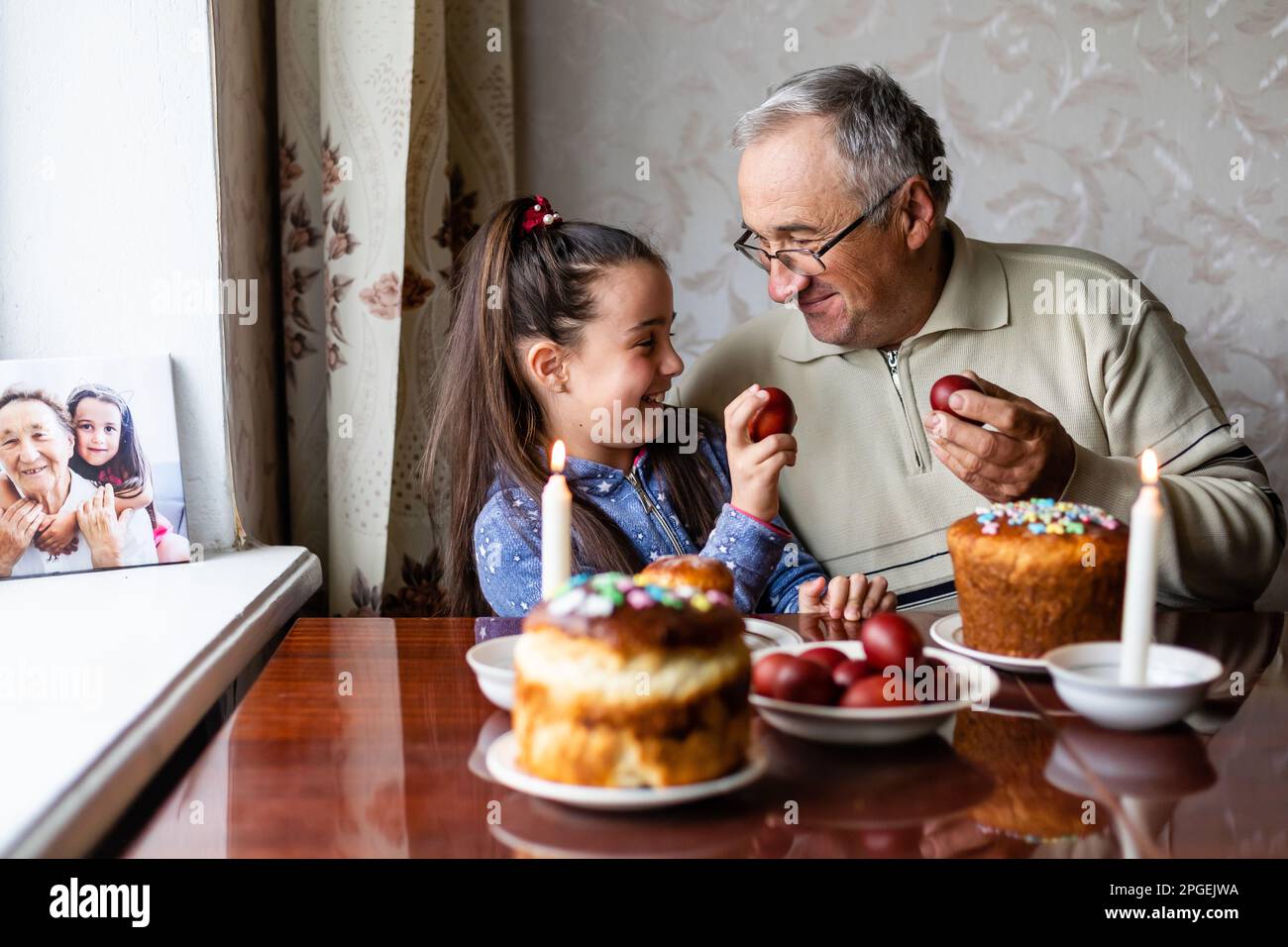 happy grandfather and granddaughter hold easter eggs in hand, folk game