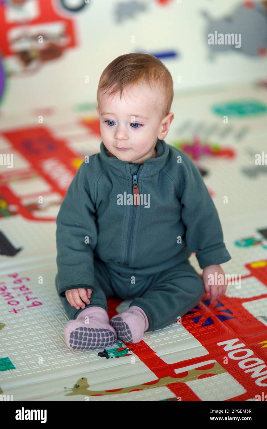 9 month old baby sitting alone on a playmat Stock Photo