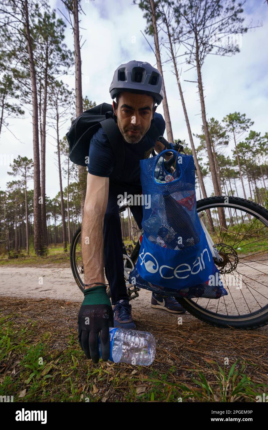Young man picking up plastic bottles and other garbage to a trash bag while practicing plogging on a bicycle through the forest Stock Photo