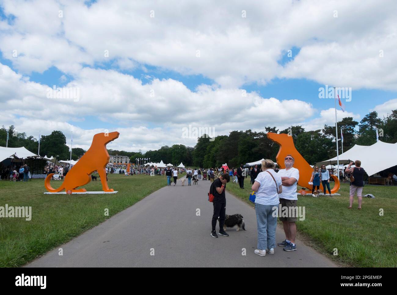 People standing next to the entrance of two orange, wooden silhouettes of hounds at Goodwoof, at The Kennels, Goodwood, West Sussex, UK Stock Photo