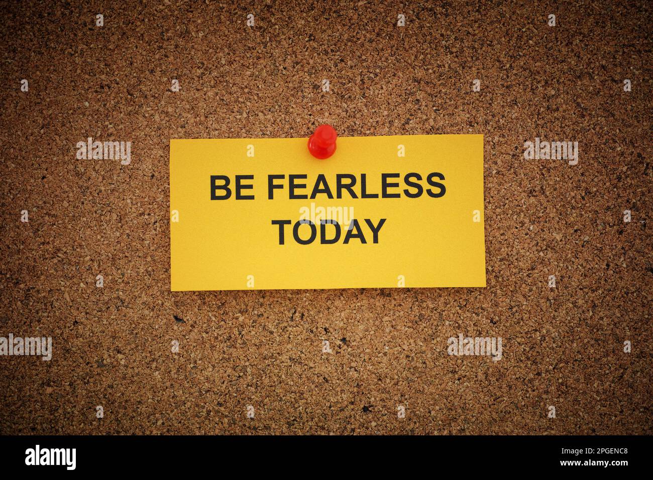A yellow paper note with the phrase Be Fearless Today on it pinned to cork board. Close up. Stock Photo