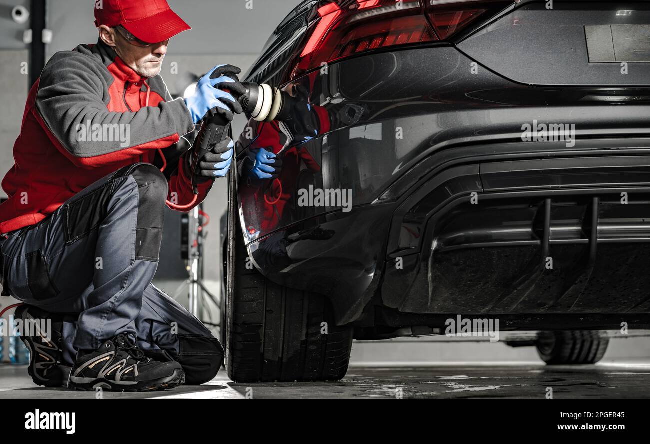Car Detailing Worker Removing Water From a Car Body Using Soft Cloth. Preparing For a Wax. Modern Vehicle Rear View. Stock Photo