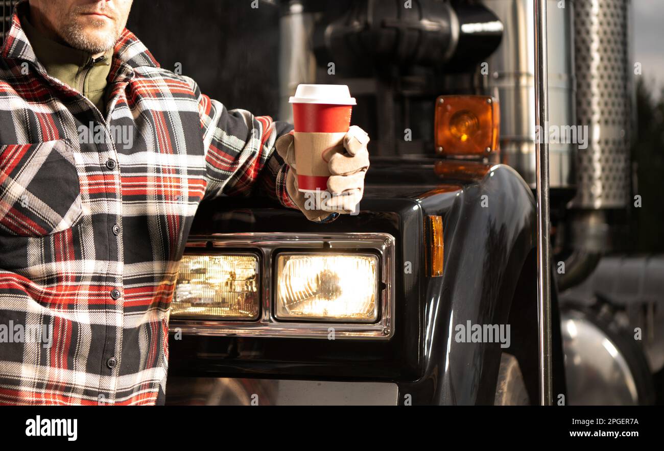 Truck Stop Coffee Break. Caucasian Trucker Drinking Hot Drink in Front of His Semi Truck Tractor. Transportation Industry Theme Stock Photo