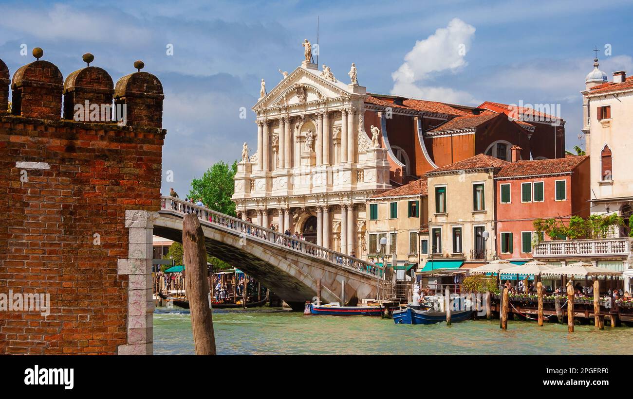 Sightseeing in Venice. Tourists cross Scalzi Bridge on Grand Canal next to the railway station, with beautiful St Mary of Nazareth Church Stock Photo