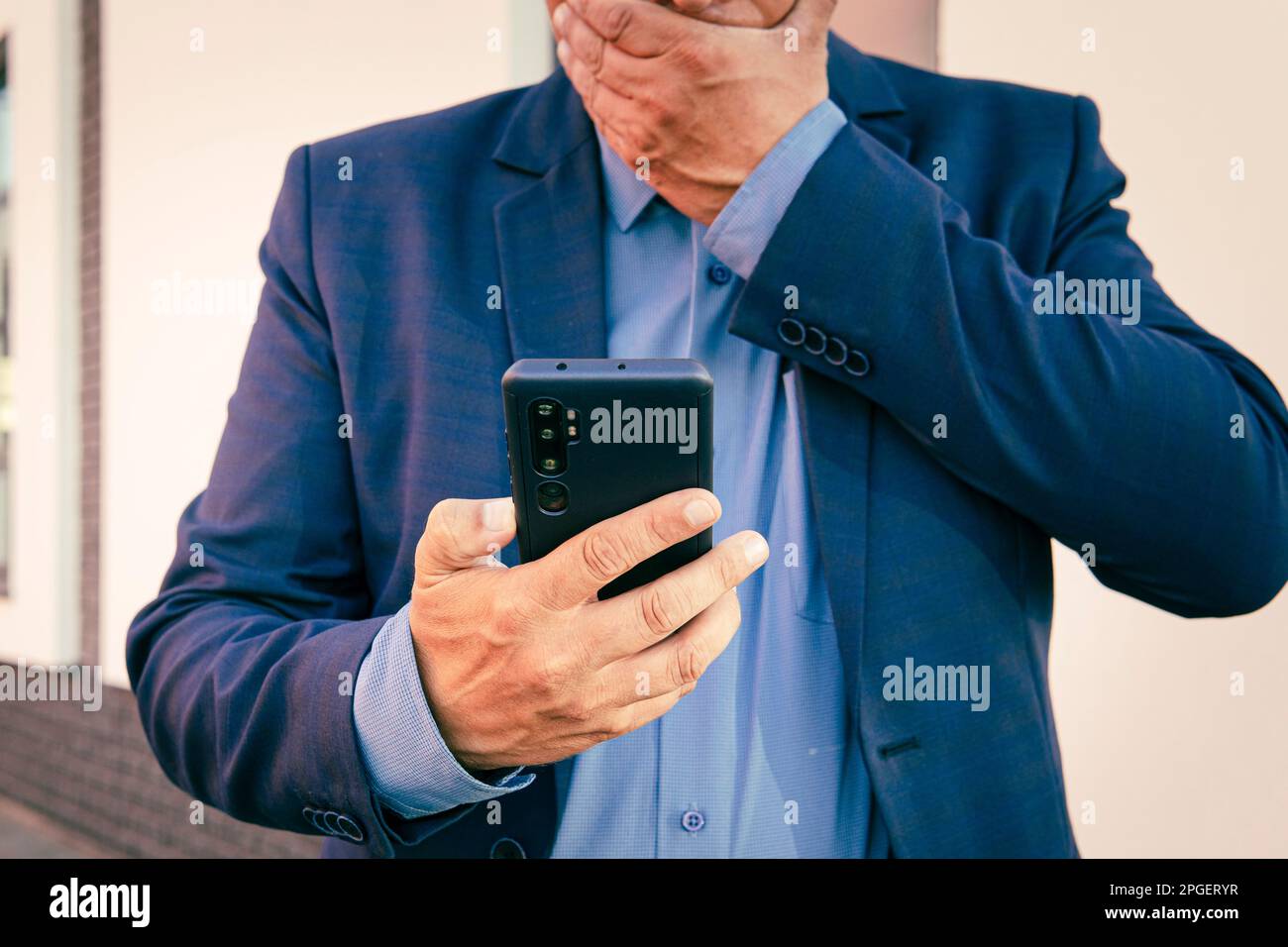 Surprised man is holding phone and reading message pointing on it with finger. A business man in a blue suit looks at a smartphone in his hand. The co Stock Photo