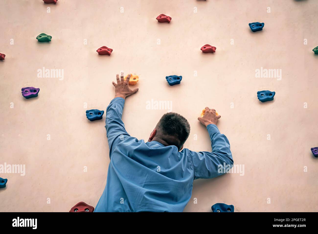 Businessman with cravat climbing a rock. Rock climbing as a hobby. an office worker trains in the gym. Extreme sports. Stock Photo