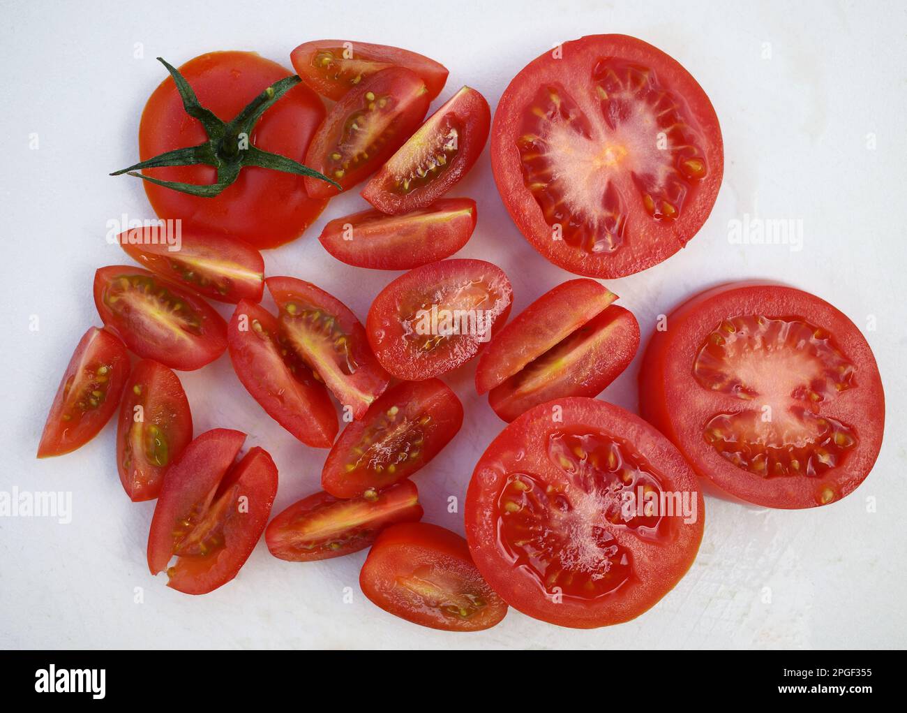 Sliced ​​red tomato combined with quartered cherry tomatoes on a white cutting board Stock Photo