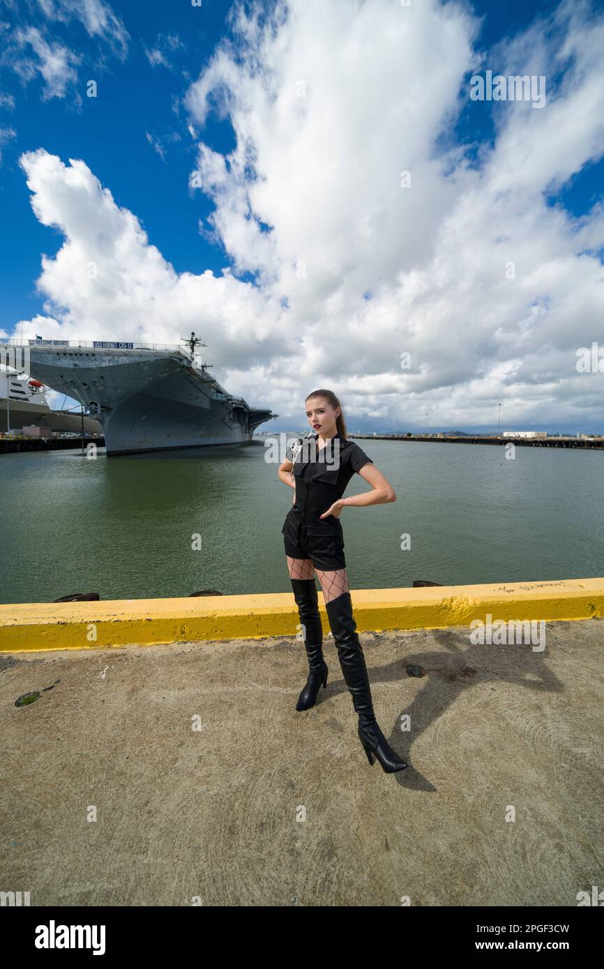 Fit Young Woman in Black Romper on Pier in Front of USS Aircraft Carrier | USS Hornet Stock Photo