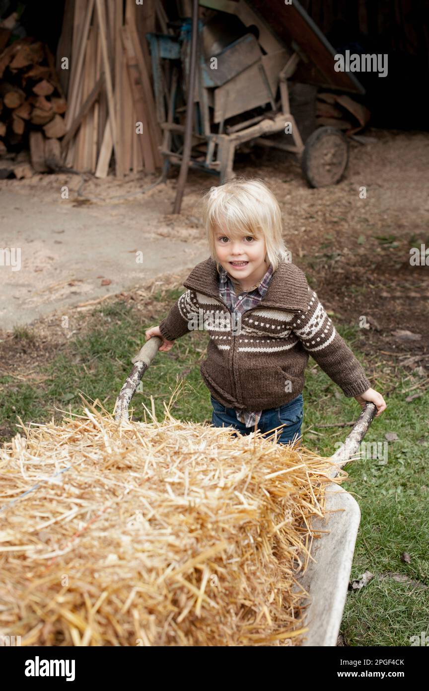 Portrait of a little boy pushing wheelbarrow in the farm, Bavaria