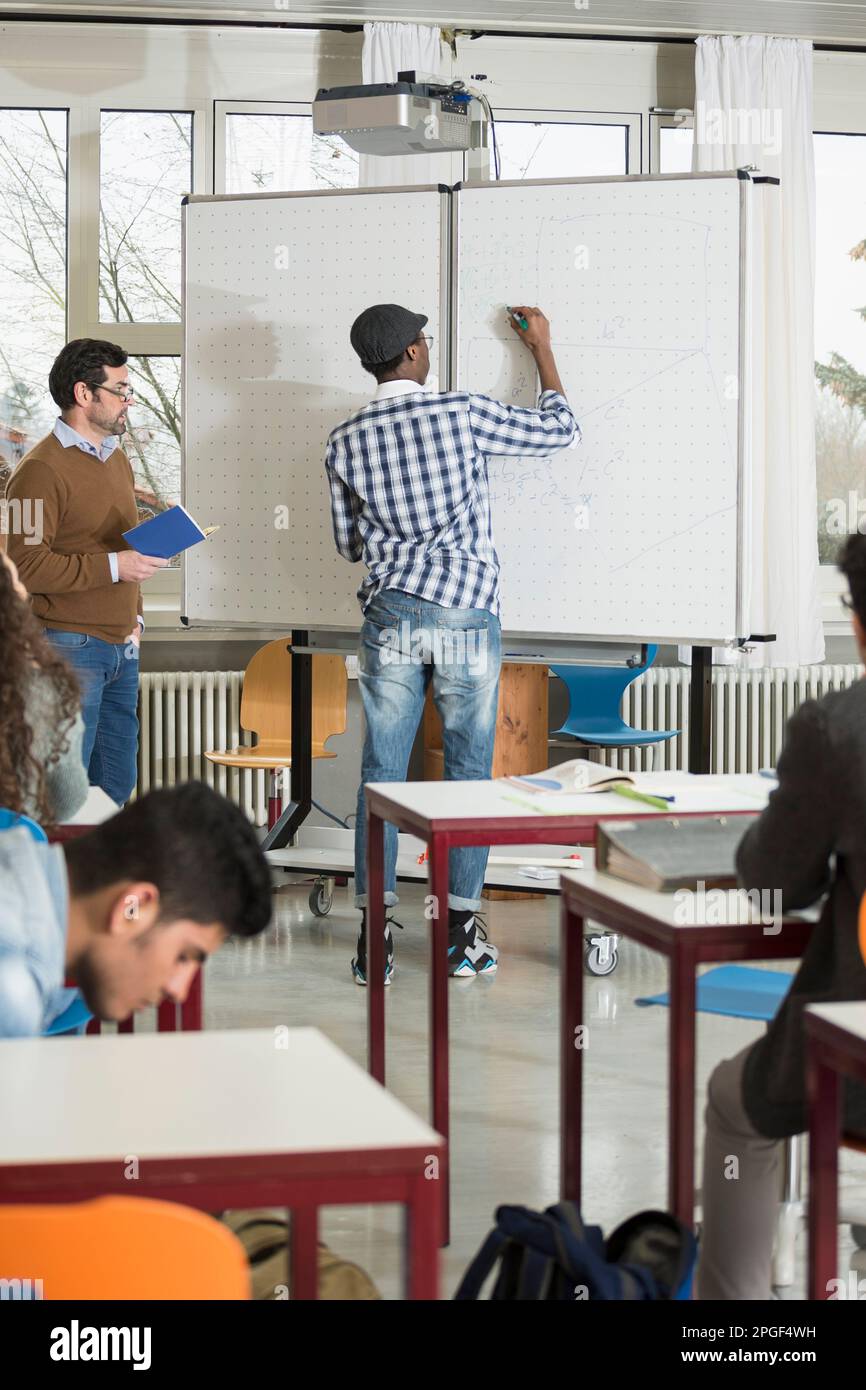Student writing on whiteboard and teacher watching him School, Bavaria, Germany Stock Photo