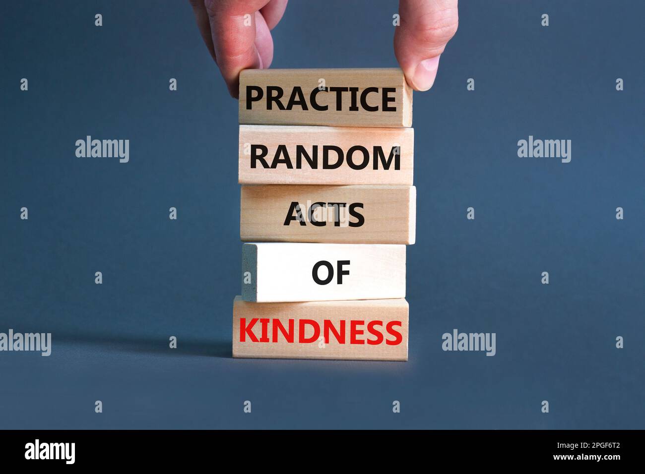 Practice random kind of kindness symbol. Concept words Practice random kind of kindness on wooden block. Beautiful grey background. Businessman hand. Stock Photo