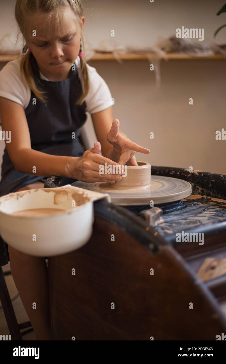 The girl creating clay mug while sitting by Potter's wheel in wo Stock Photo