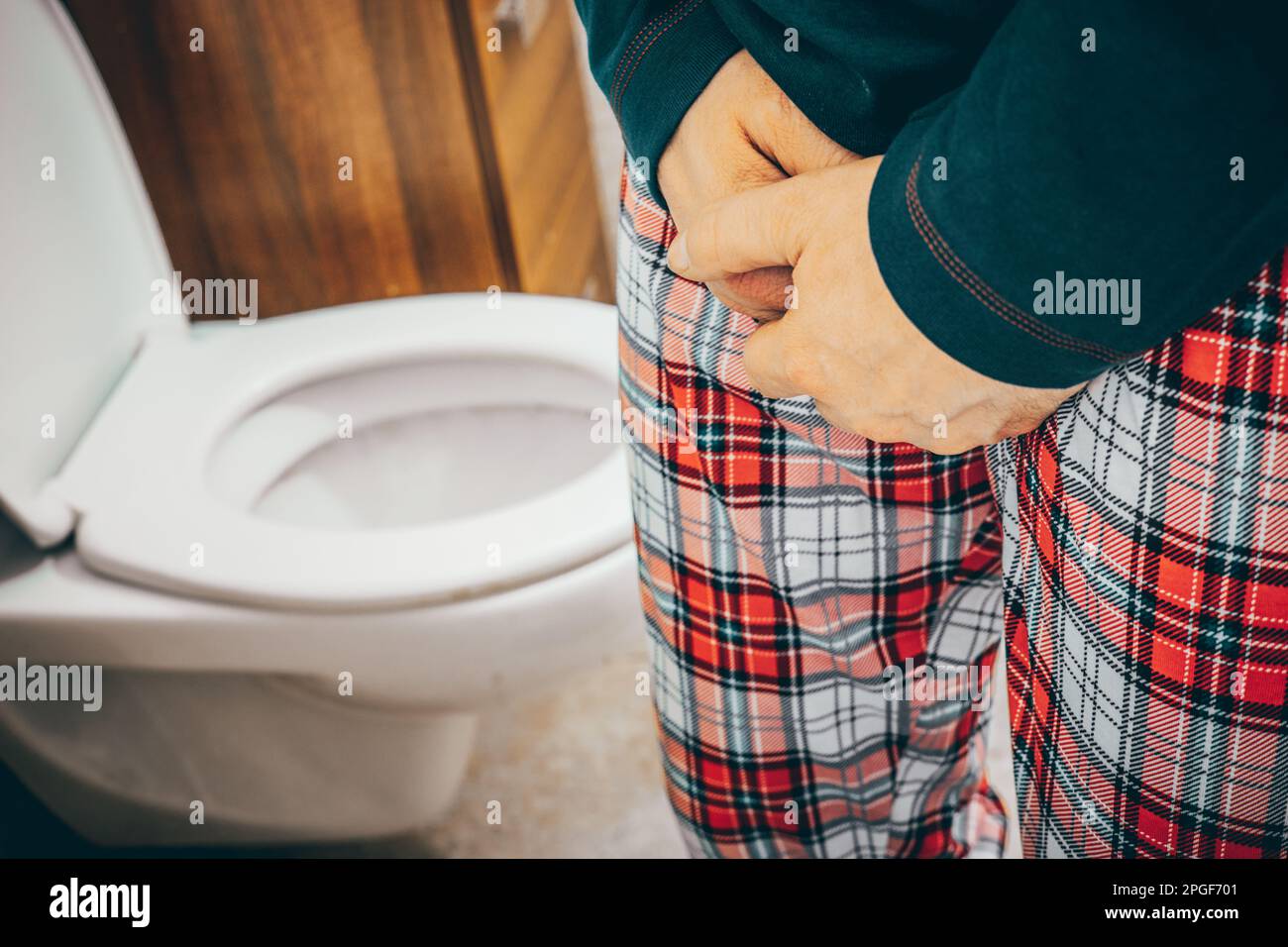 A man in pajamas in the toilet squeezes his crotch and lifts the toilet