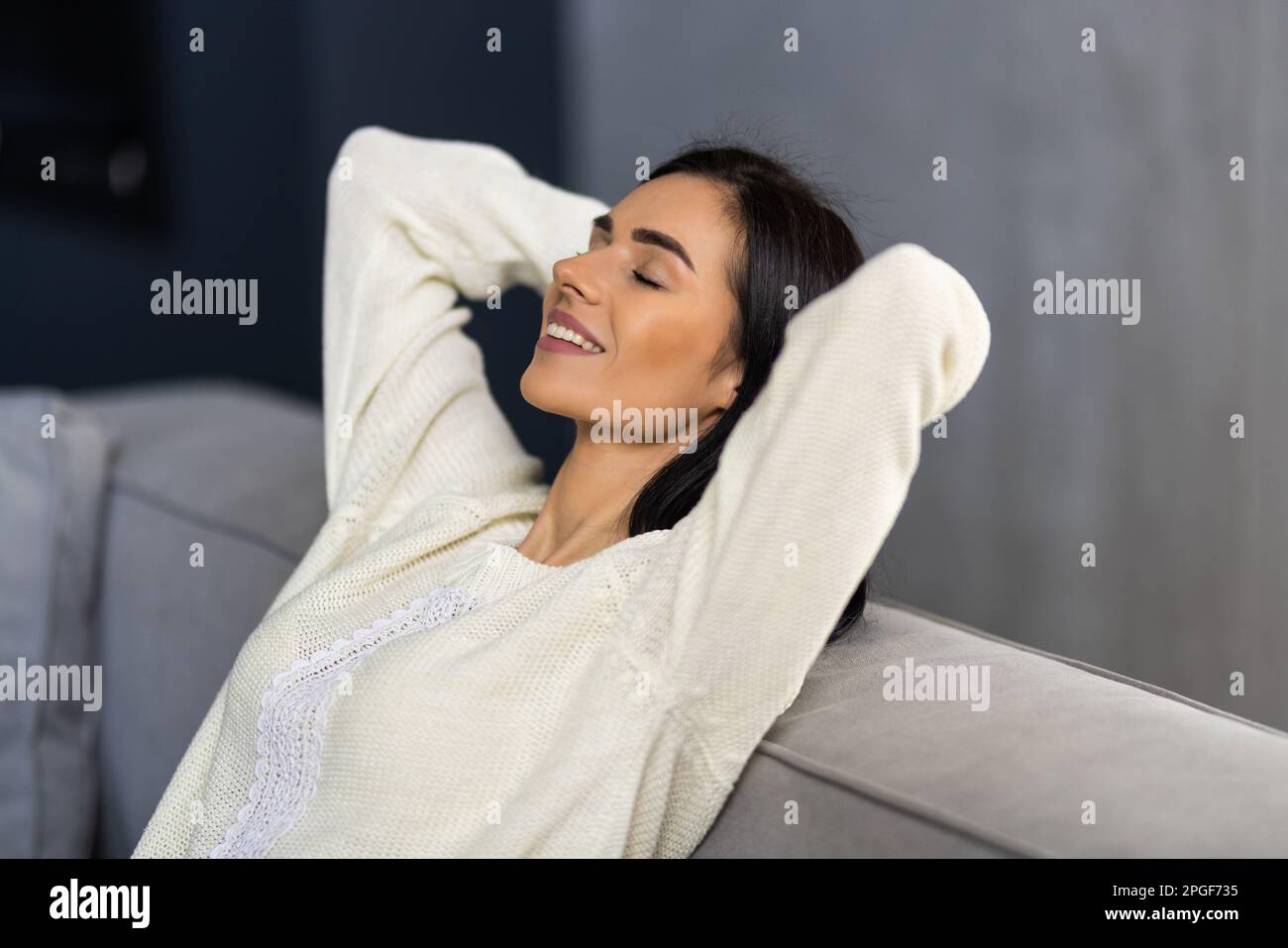 Kick back and relax concept. Young beautiful brunette woman with blissful facial expression alone on the couch with her bare feet on coffee table. Por Stock Photo