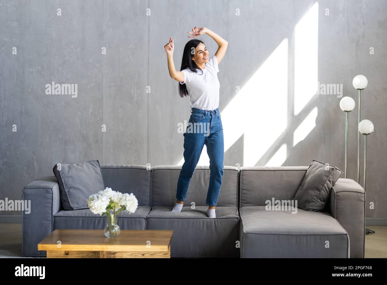 Shot of funny woman listening to music with smartphone while dancing on the couch in the living room at home. Stock Photo