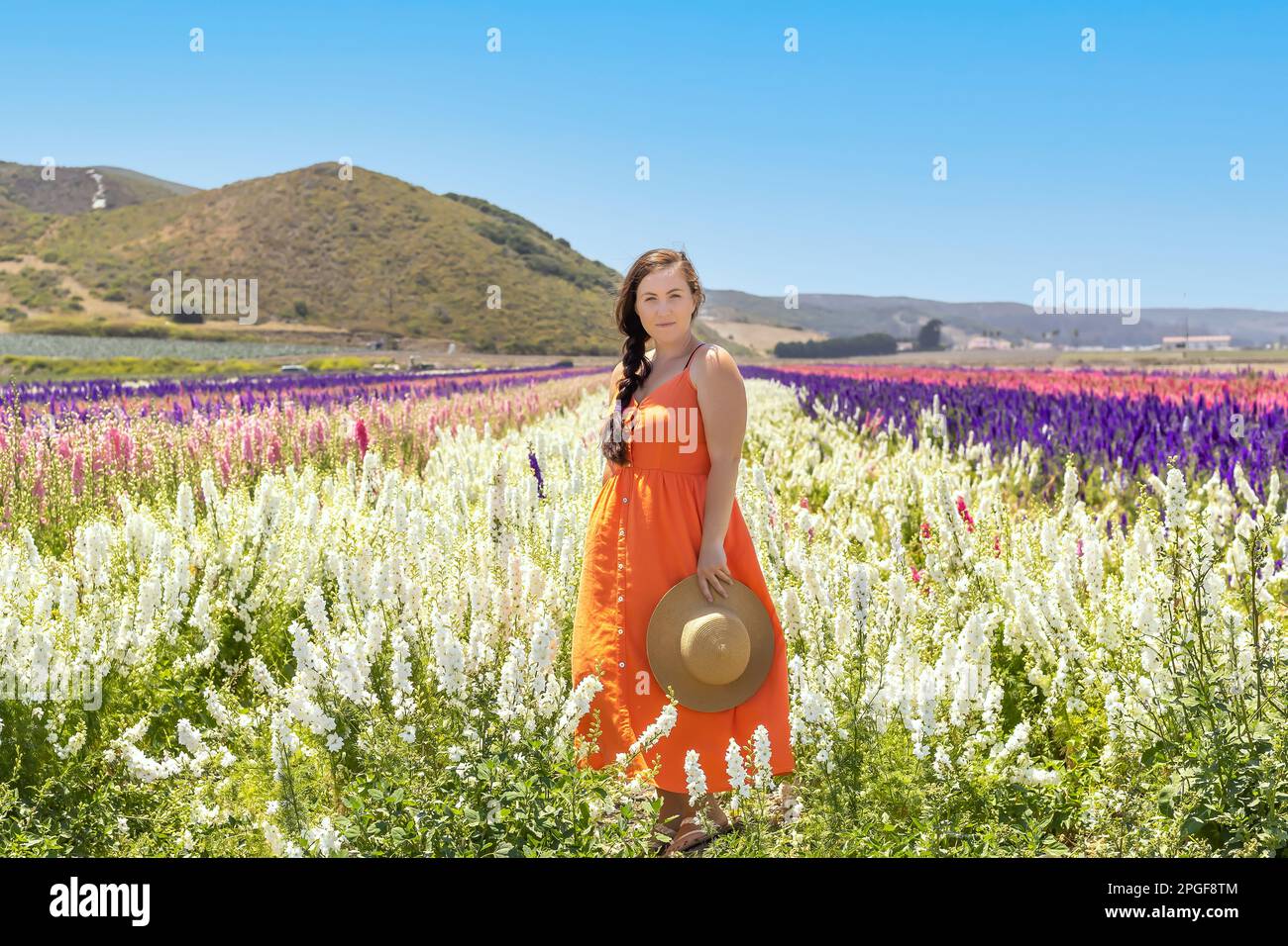 Woman in orange dress looking at camera, stood in flower field Stock Photo