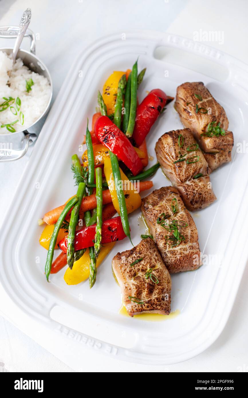 Fresh black cod with grilled vegetables served on a large white plate Stock Photo