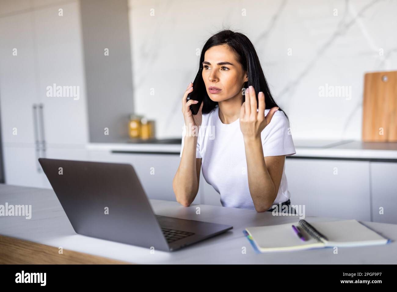 Beautiful young Caucasian woman calling bank using cell phone concerning information on credit card that she is holding. Serious female connecting to Stock Photo