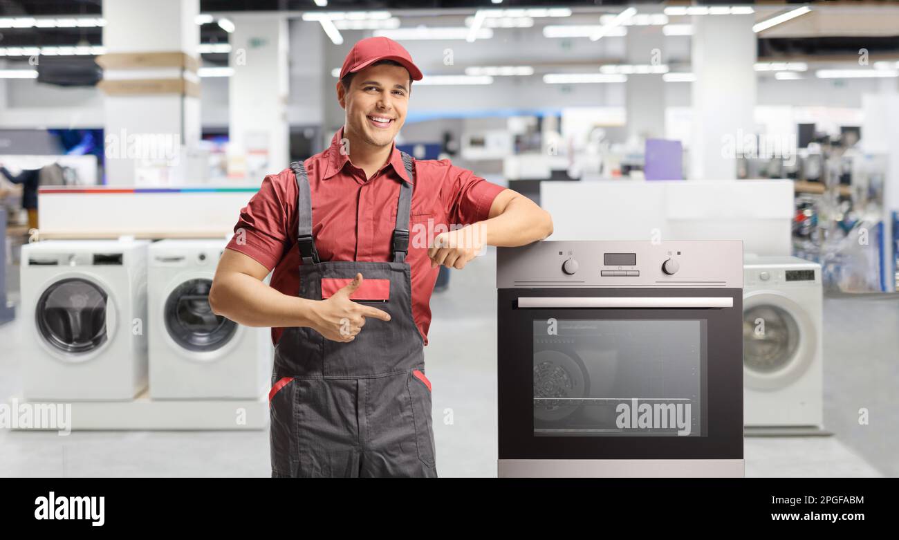 Repairman pointing at an electric oven inside an appliance shop Stock