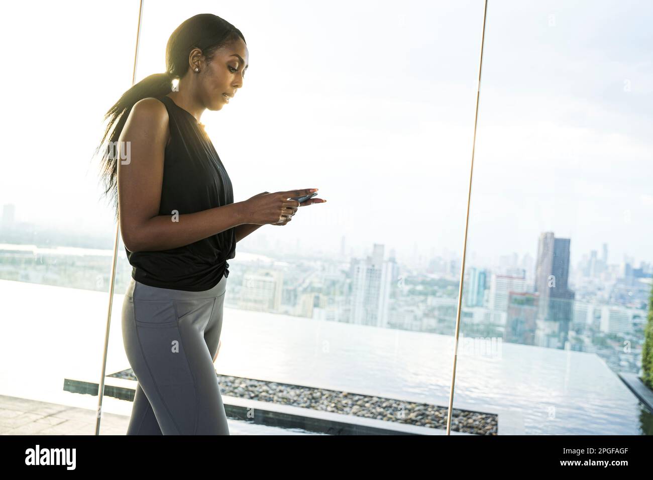 Athletic black woman using her  phone outdoors panoramic city view. Stock Photo