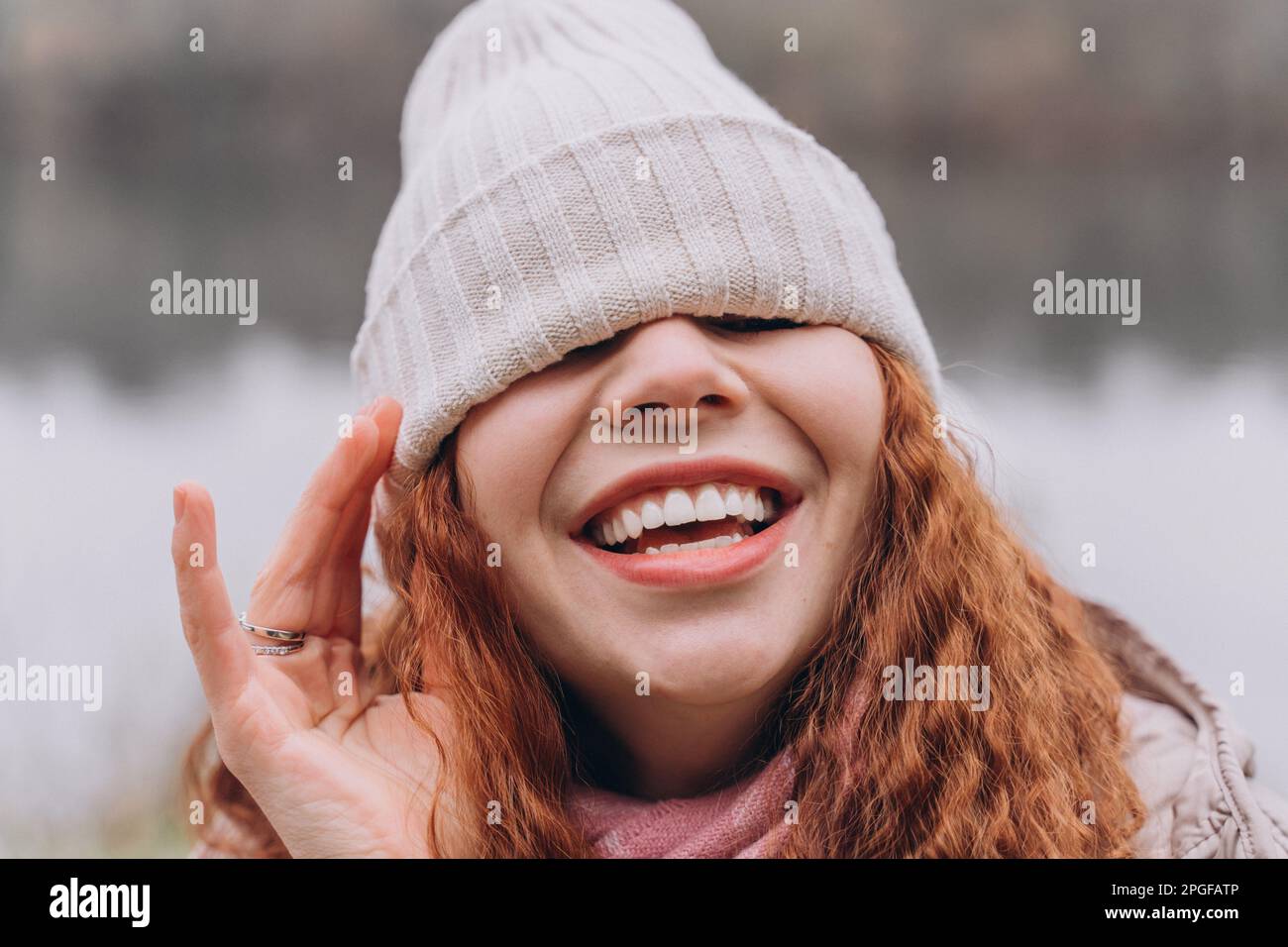 Curly redhead woman 30-35 with a cap over her eyes laughs Stock Photo