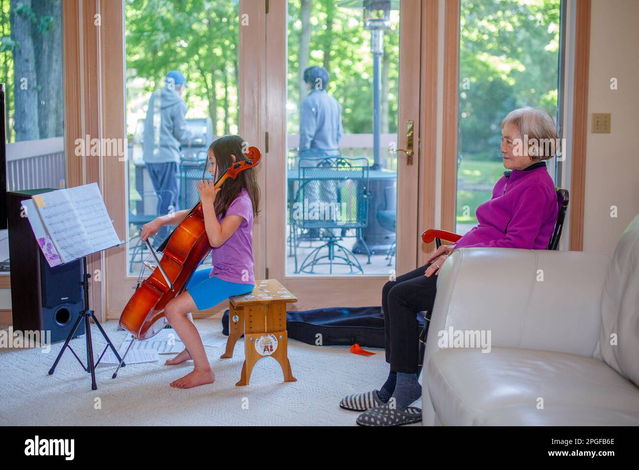 A little girl gives cello concert to grandmother inside Stock Photo