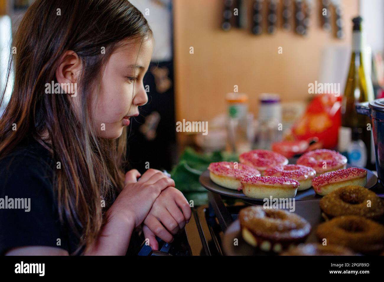 A little girl stares longingly at donuts on countertop Stock Photo