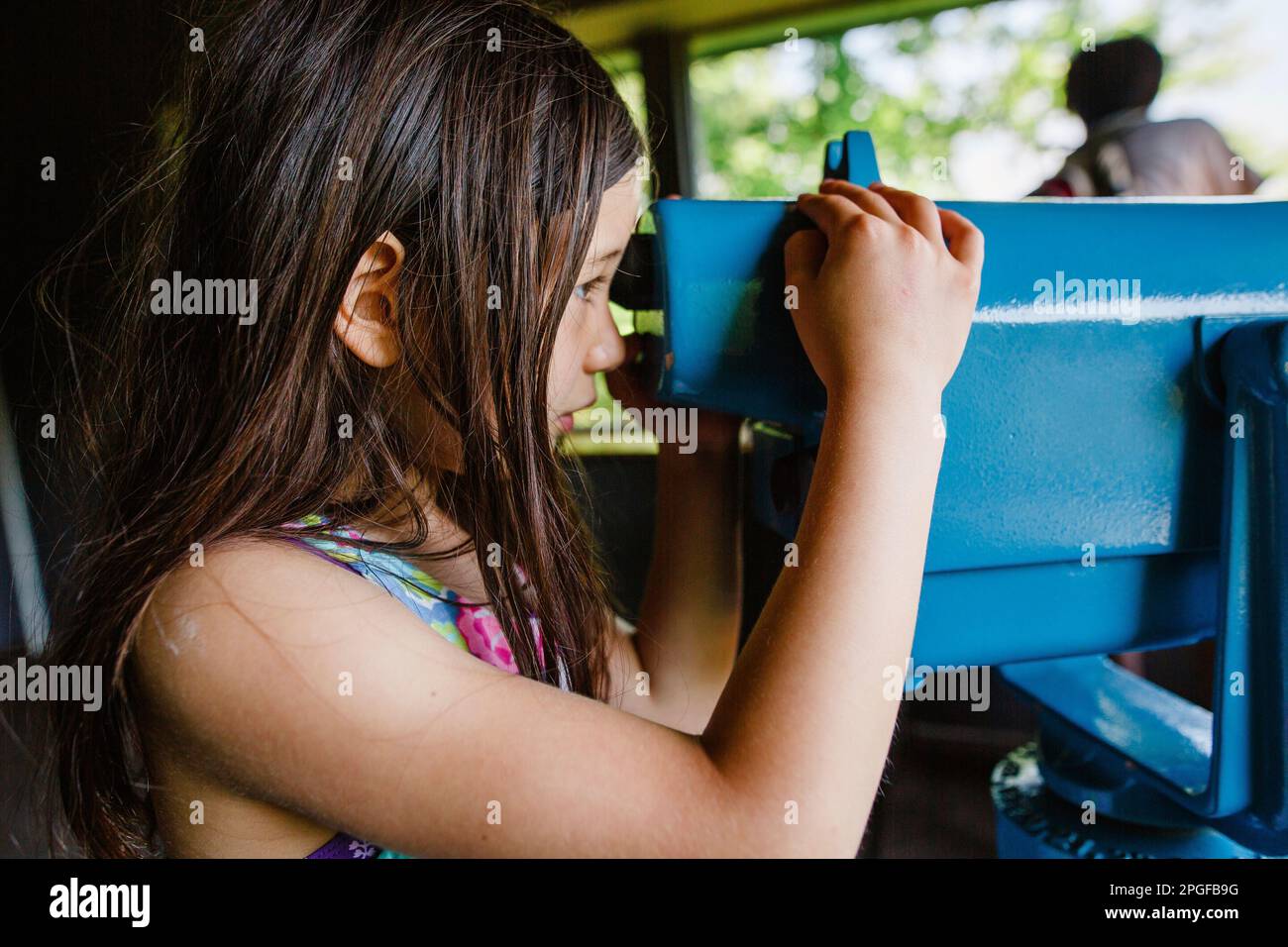 Side-view of a girl studying nature through large binoculars Stock Photo