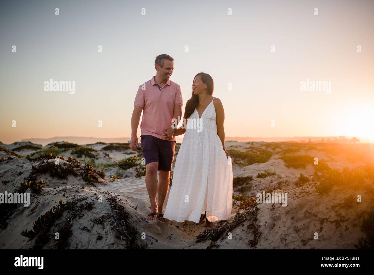 Husband & Pregnant Wife Holding Hands on Beach at Sunset in San Diego Stock Photo