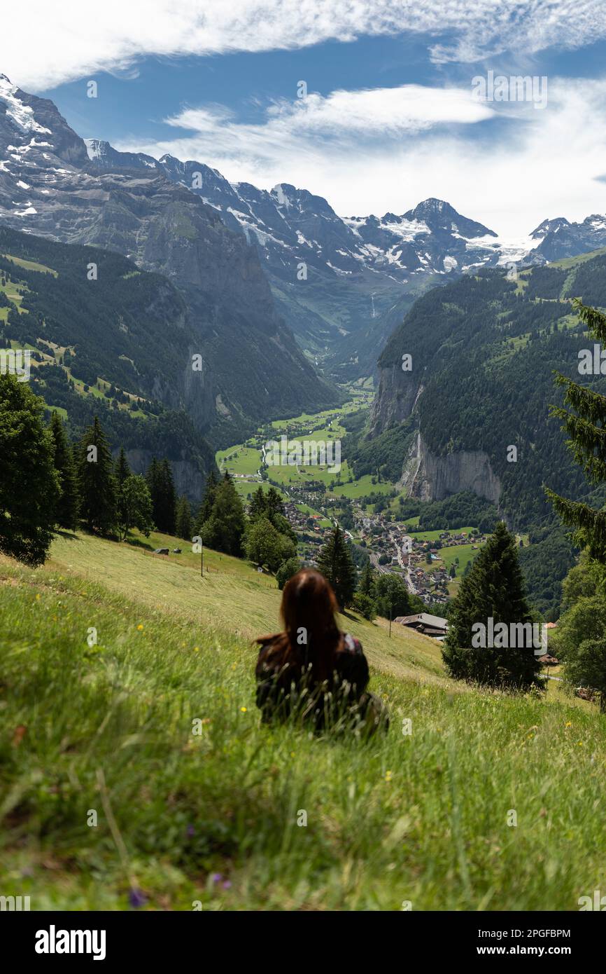 Woman Sitting In The Meadow Looking At Lauterbrunnen Valley Stock Photo