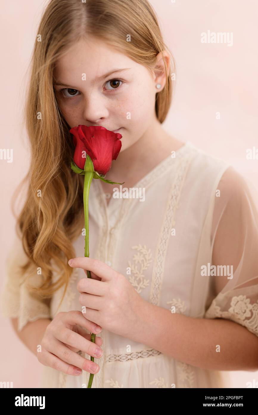 Young girl holding smelling a red rose against pink backdrop Stock Photo