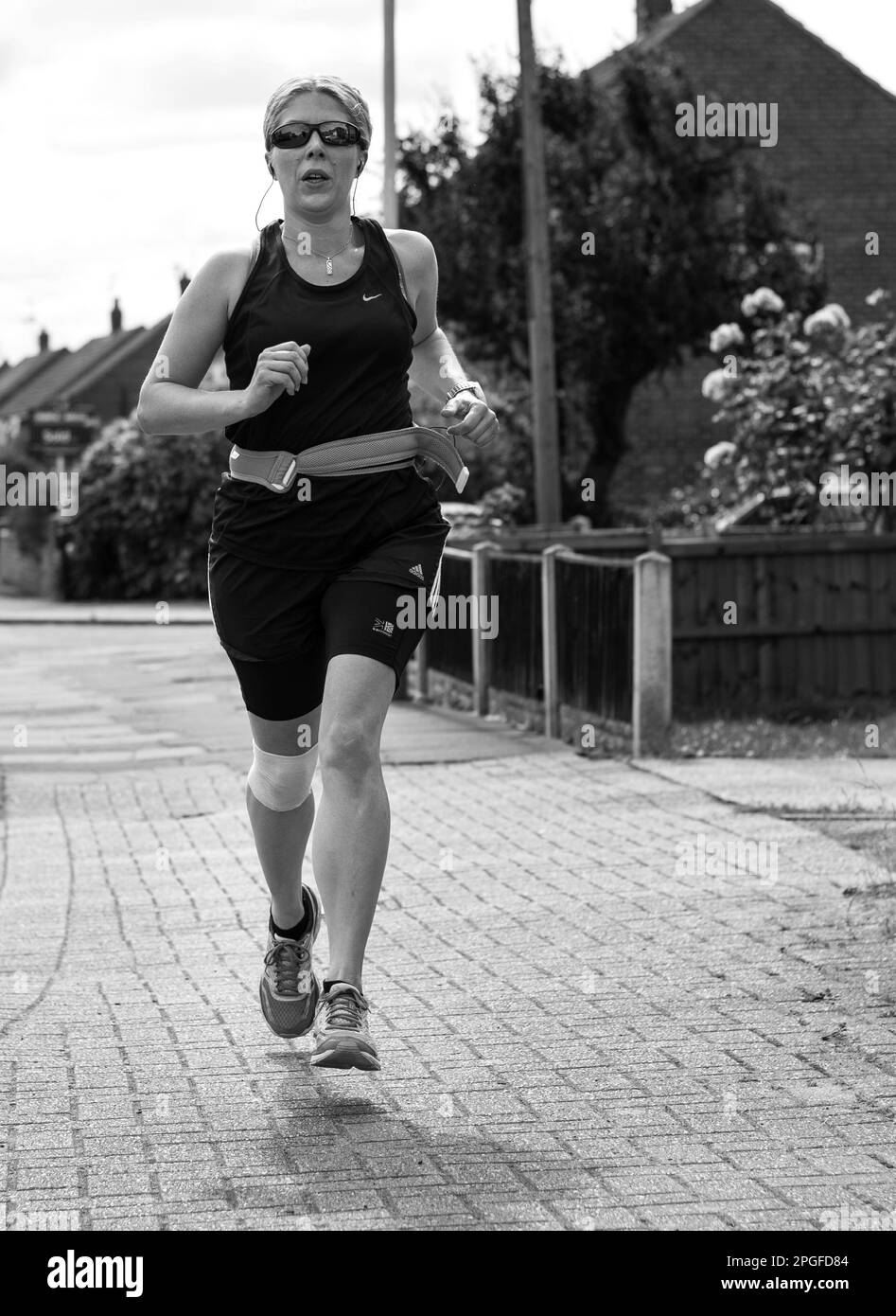 Black and white image of a female runner, running down a street Stock