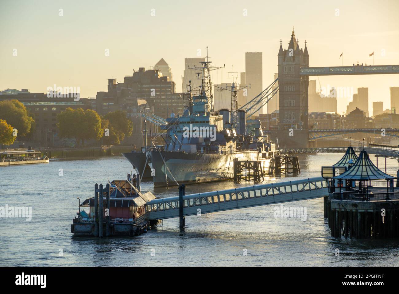 HMS Belfast and ship alongside with Tower Bridge behind at dusk, London, UK Stock Photo