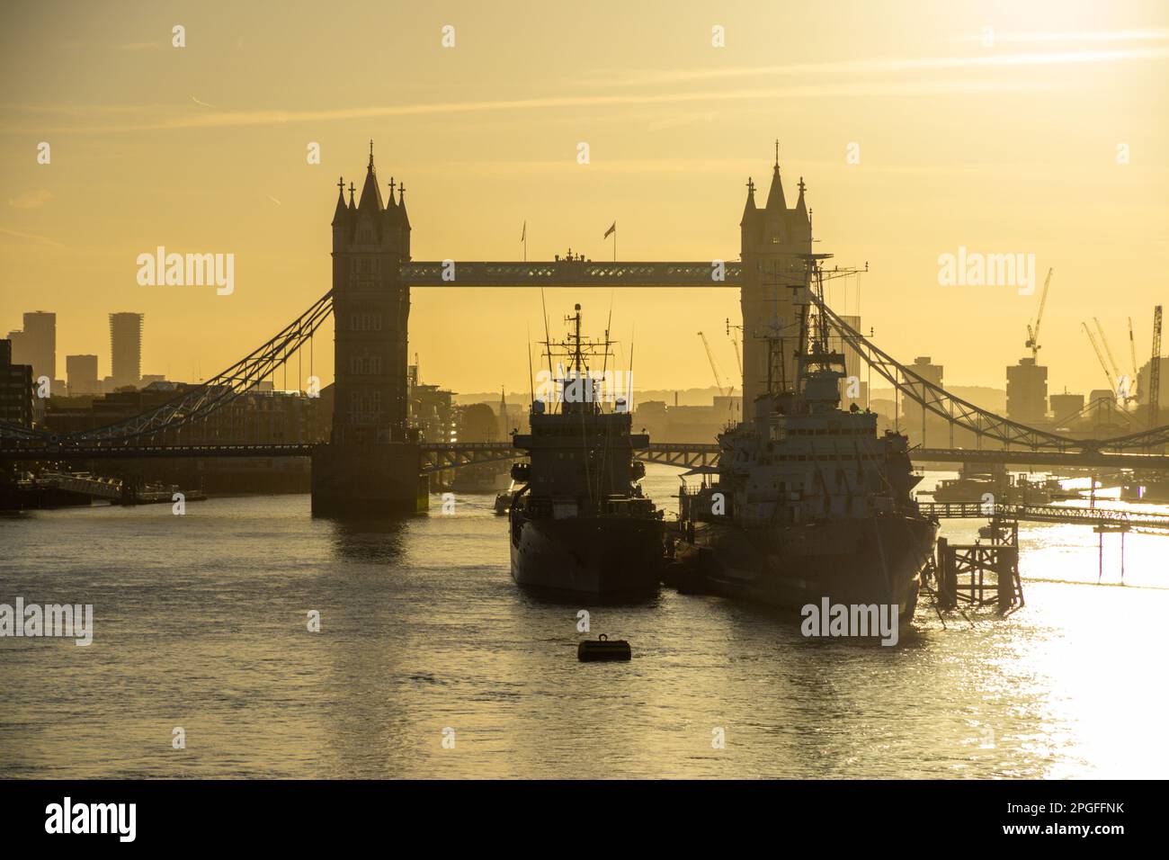 HMS Belfast and ship alongside with Tower Bridge behind at dusk, London, UK Stock Photo