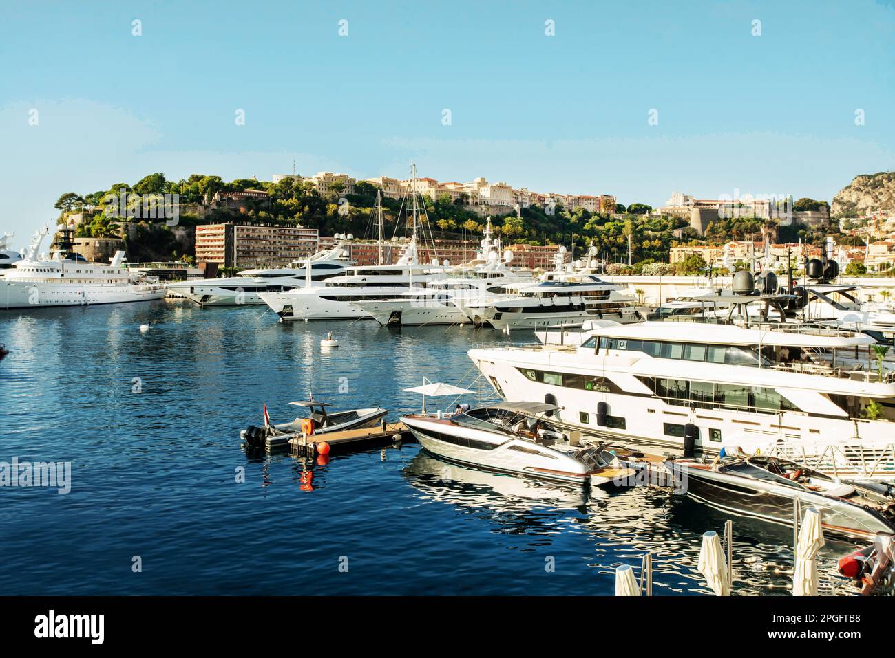 Idyllic view of the harbor (Port Hercule) of Monaco with luxury yachts and the skyline of Monaco. Photo from Mone Carlo, in right  upper corner: Princ Stock Photo