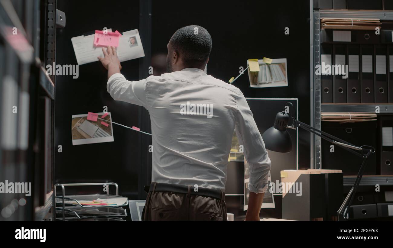 Policeman analyzing detective evidence board on wall, brainstorming to
