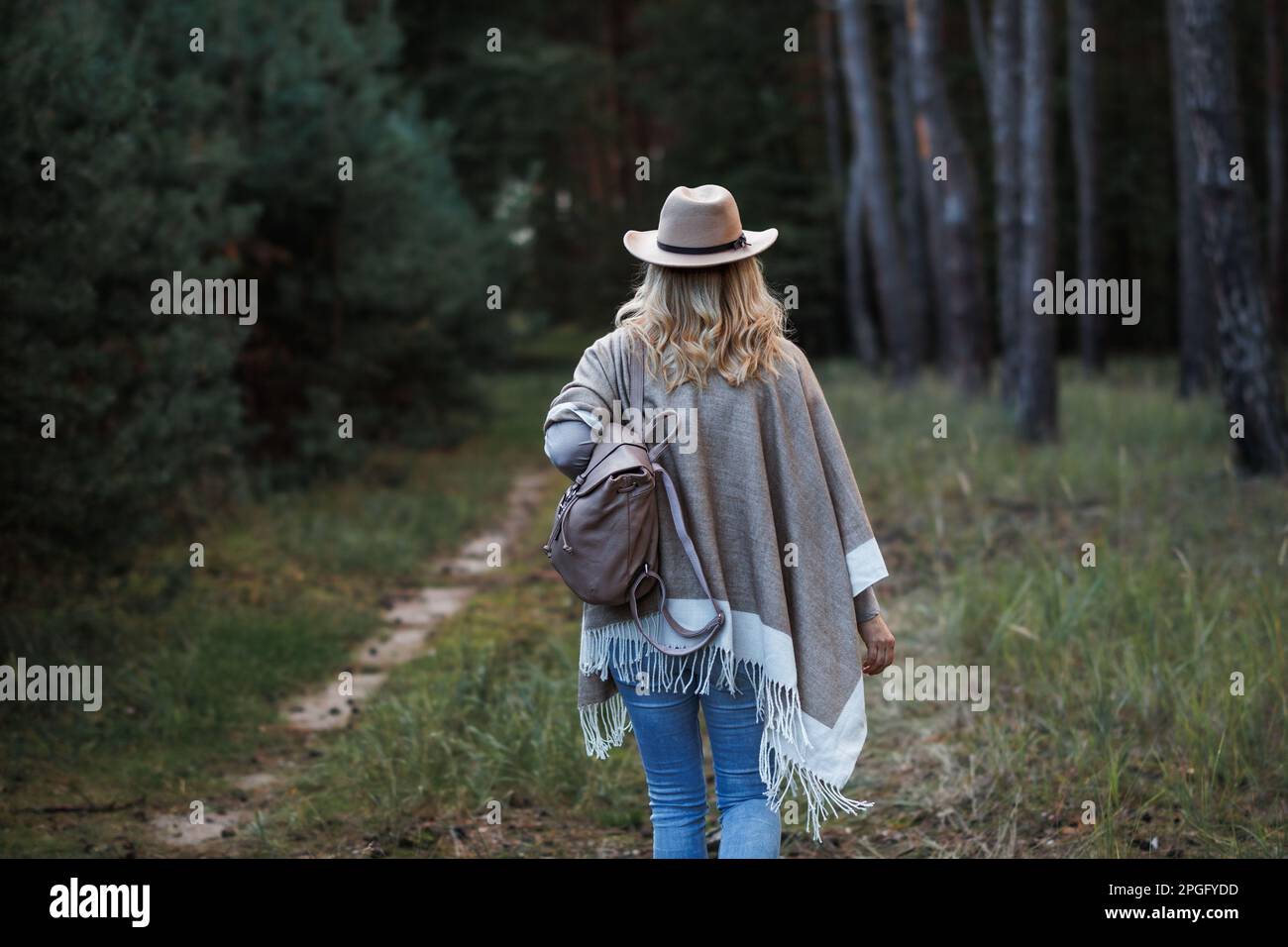 Woman with poncho, cowboy hat and backpack walking in forest Stock Photo