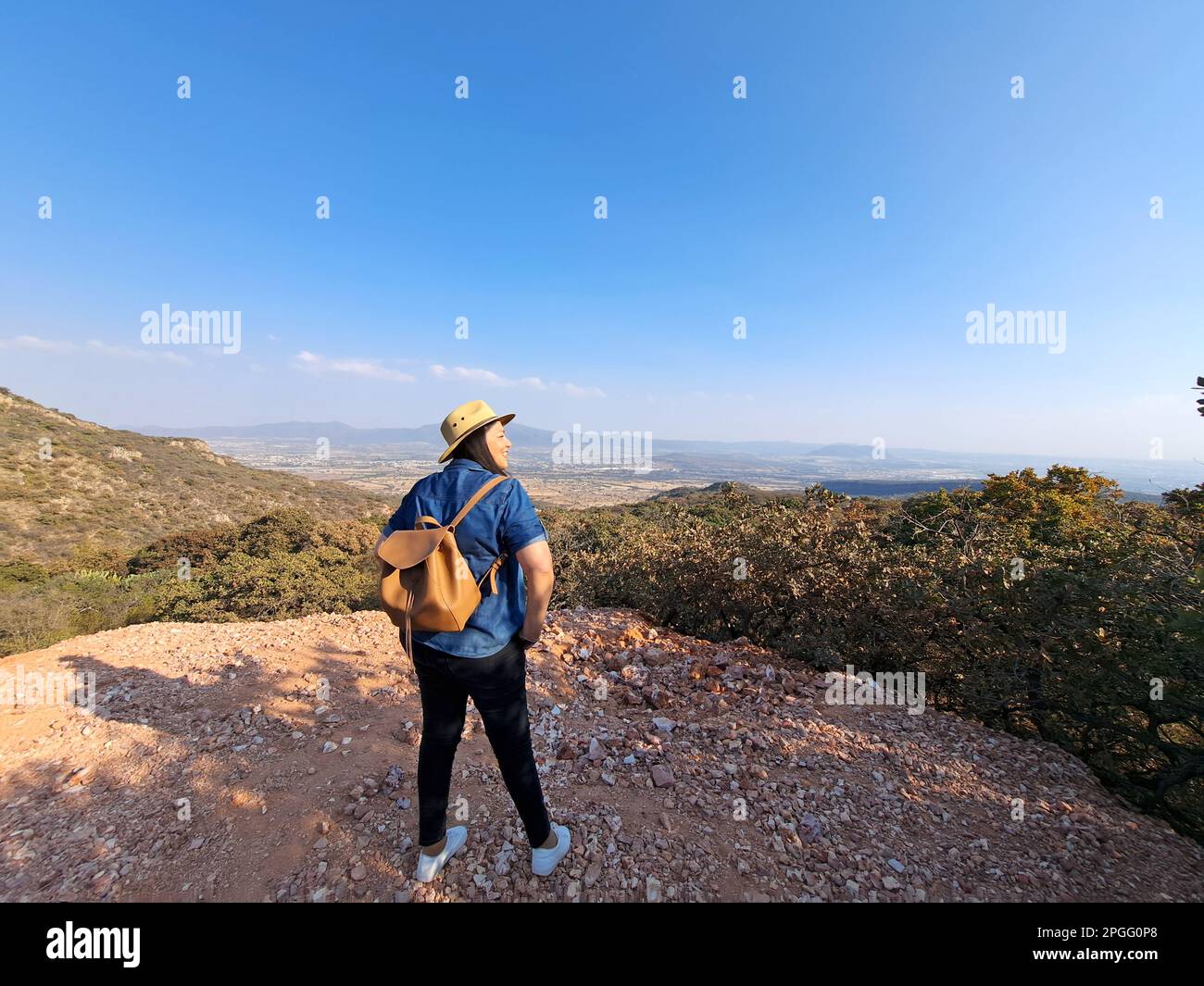 Adult woman with hat looks towards the horizon on top of a mountain ...