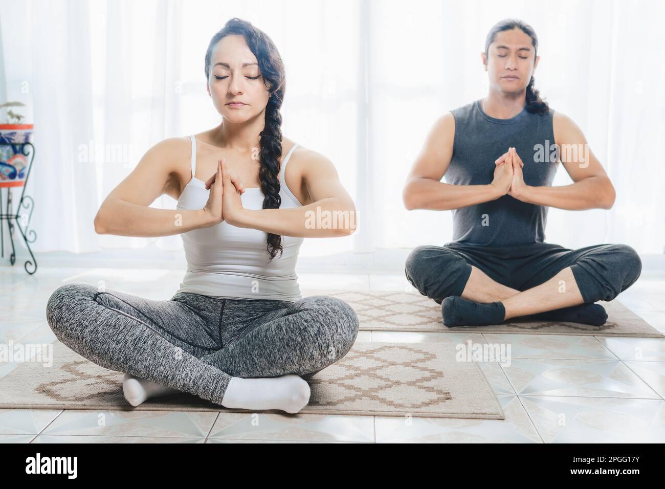 Two middle-aged people are doing Yoga indoors, with lots of sunlight coming in through the window, doing deep meditation positions. There is a lot of Stock Photo