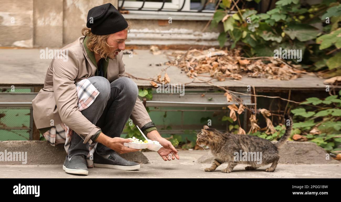 Poor man sharing food with homeless cat outdoors Stock Photo